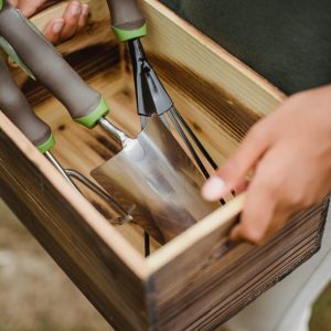 Personalized Gardening Kits a wooden box filled with gardening tools. The box contains a trowel, a hand fork, and a weeder, all with gray handles and green accents.